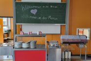 Eine Speisenausgabe mit einer Tafel im Hintergrund, auf der "Willkommen in der Mensa" steht.