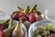 Drei Obstkörbe stehen nebeneinander. Darin sind Äpfel, Bananen, Birnen und Weintrauben.