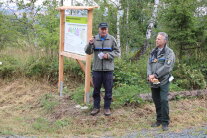 Zwei Männer in Dienstkleider stehen im Wald vor einem Schild