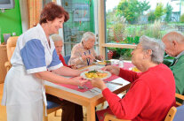 Frau reicht Seniorin Teller mit Essen