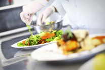 Hände mit Schutzhandschuhen trapieren Salat auf Teller © Getty RF